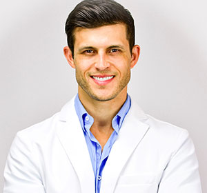 Headshot of Dr. Chris Strandburg, indoors, with short brown hair, wearing a white coat and blue shirt