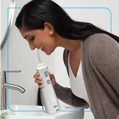 Woman in bathroom using a Waterpik cordless handheld water flosser