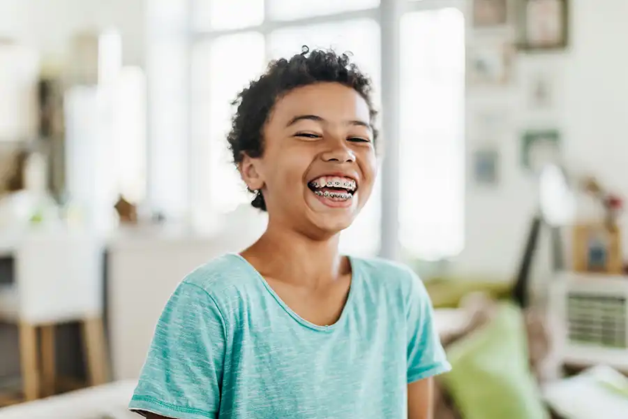 Boy with blue t-shirt and braces smiling.