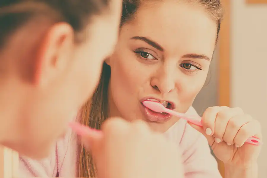 Woman brushing teeth, looking in mirror