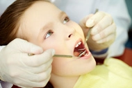 Dentist examining a child's teeth using dental instruments.