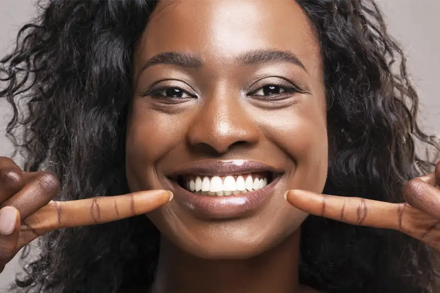 Woman with dark curly shoulder length hair smiling and pointing to her teeth