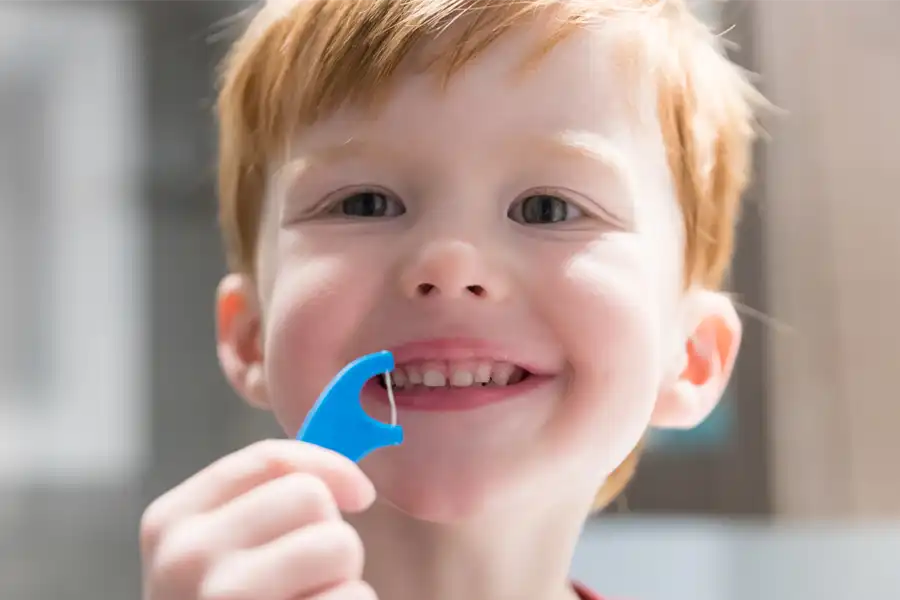 Young boy with red hair holding dental floss pick while smiling