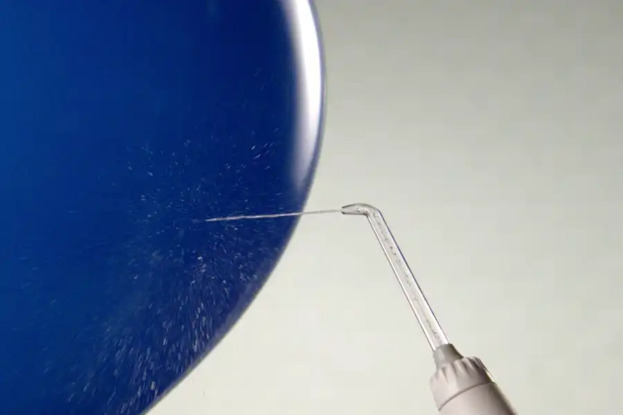 Blue balloon with the words Powerful Yet Gentle! with a Waterpik™ water flosser handle and tip shooting water against it