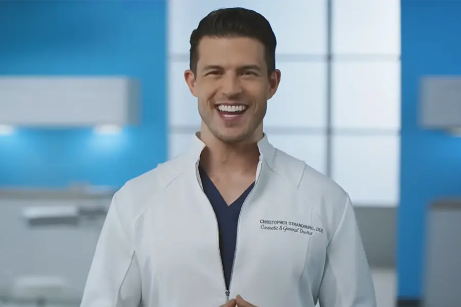 Dentist Dr. Chris Strandburg, smiling, wearing a white lab coat and black shirt