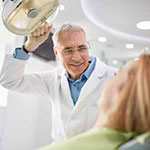 Dental professional holding light over woman in dentist chair