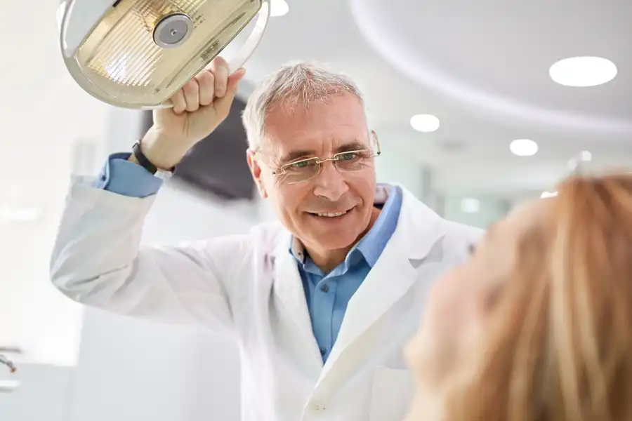 Dental professional holding light over woman in dentist chair