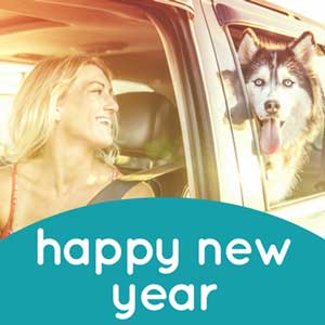 Image of woman with long blonde hair, wearing red tank top, smiling and looking over shoulder at large dog in backseat
