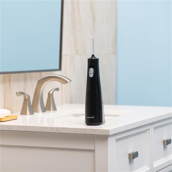 Black Cordless 1100 handheld water flosser on a bathroom sink.