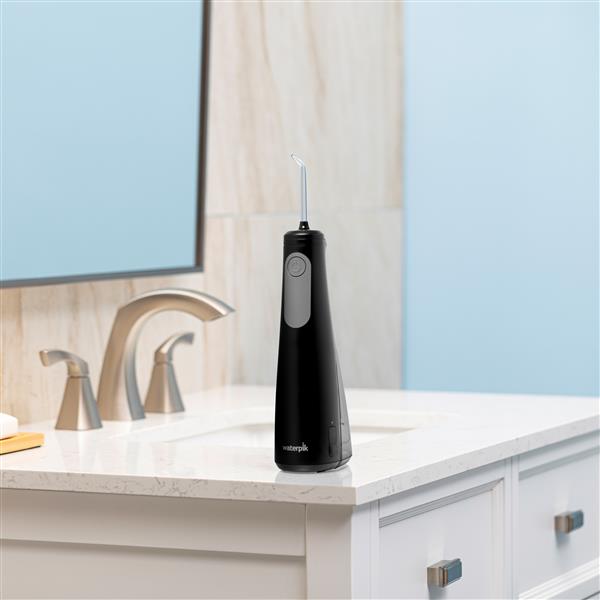 Black Cordless Enhance 3200 handheld water flosser on a bathroom sink.