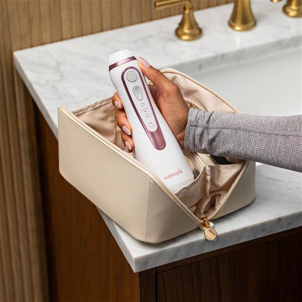 Rose Gold Cordless Advanced 2.0 handheld water flosser, without tip, taken out of a toiletry bag.