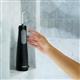 Black Cordless Enhance 3200 water flosser on a shower ledge, with a hand reaching for it.
