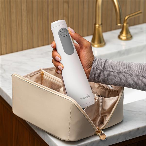 White Cordless Enhance 3200 handheld water flosser, without tip, taken out of a toiletry bag.