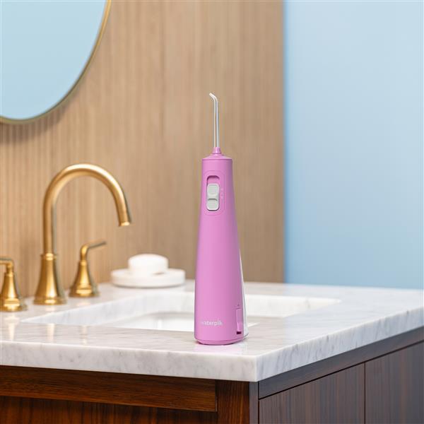Mauve Cordless Pulse 3100 handheld water flosser on a bathroom sink.