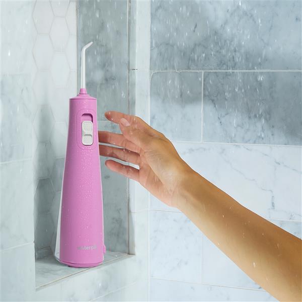 Mauve Cordless Pulse 3100 water flosser on a shower ledge, with a hand reaching for it.
