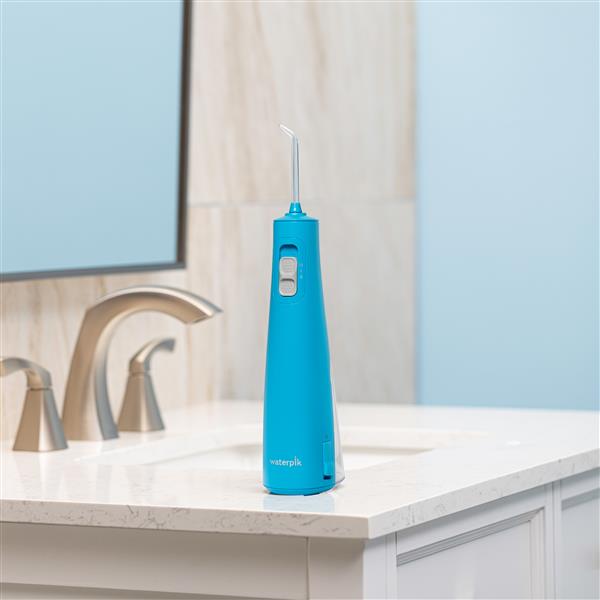 Cyan Cordless Pulse 3100 handheld water flosser on a bathroom sink.