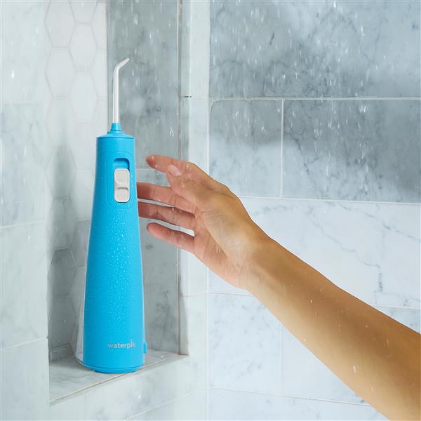 Cyan Cordless Pulse 3100 water flosser on a shower ledge, with a hand reaching for it.