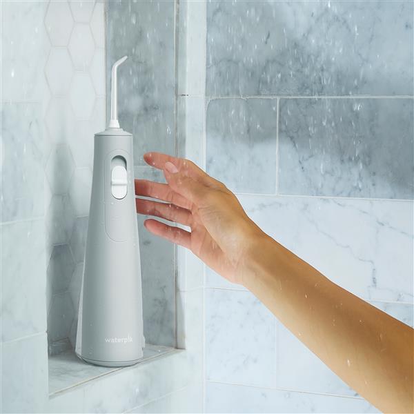 Gray Cordless water flosser on a shower ledge, with a hand reaching for it.