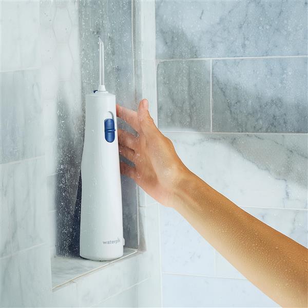 White Cordless 1000 water flosser on a shower ledge, with a hand reaching for it.