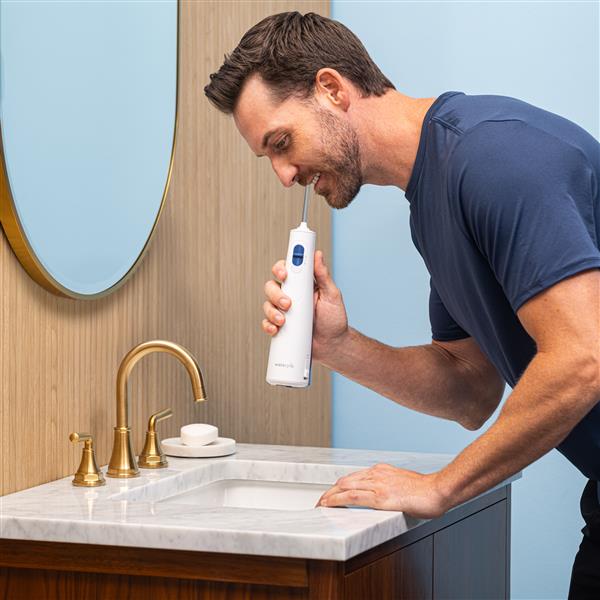 White Cordless 1200 handheld water flosser in use, with person leaning over the bathroom sink.