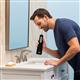 Black Cordless Enhance 3200 handheld water flosser in use, with person leaning over the bathroom sink.