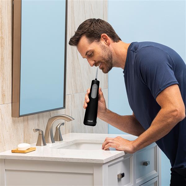 Black Cordless Enhance 3200 handheld water flosser in use, with person leaning over the bathroom sink.