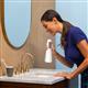 White Cordless Enhance 3200 handheld water flosser in use, with person leaning over the bathroom sink.