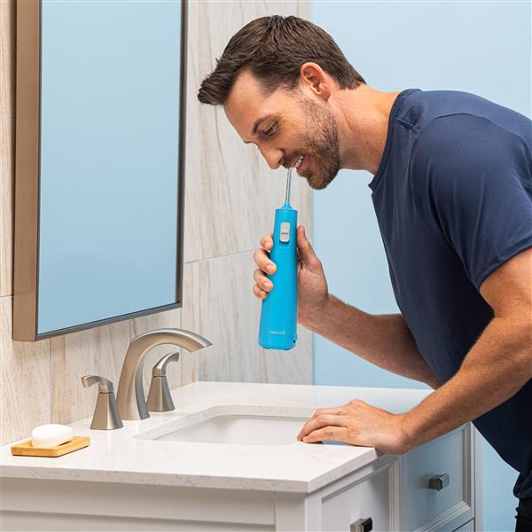 Cyan Cordless Pulse 3100 handheld water flosser in use, with person leaning over the bathroom sink.