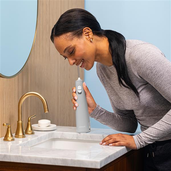 Gray Cordless handheld water flosser in use, with person leaning over the bathroom sink.