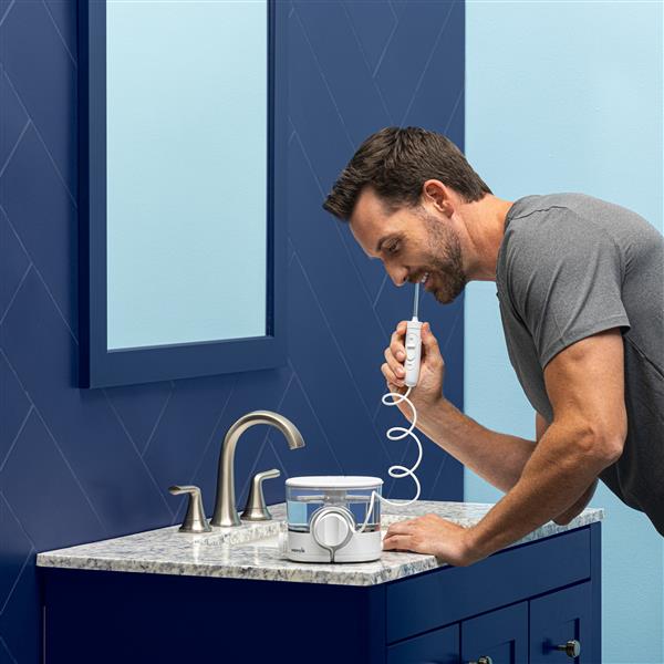 White ION countertop water flosser in use, with person leaning over the bathroom sink.