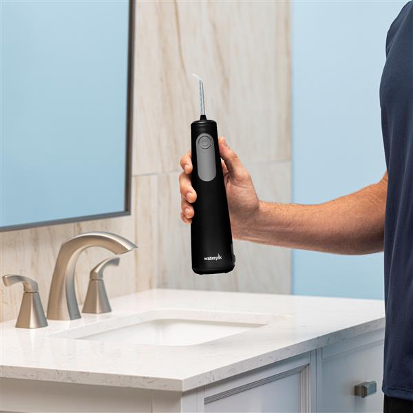 Black Cordless Enhance 3200 handheld water flosser held vertically above bathroom sink.