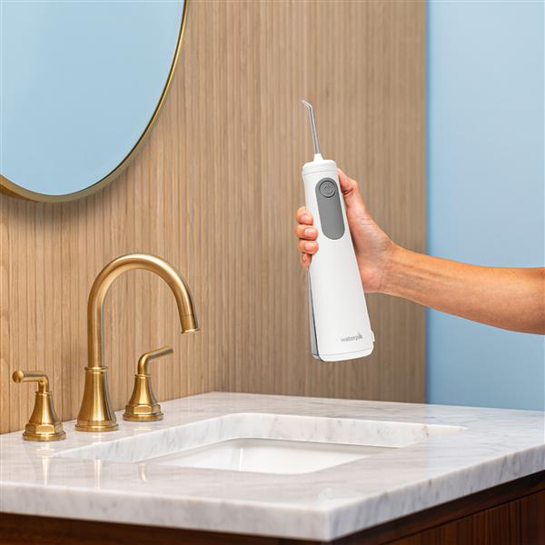 White Cordless Enhance 3200 handheld water flosser held vertically above bathroom sink.