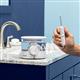 White ION countertop water flosser on a bathroom sink, with hand holding the handle and attached tip, extended by its coiled hose.