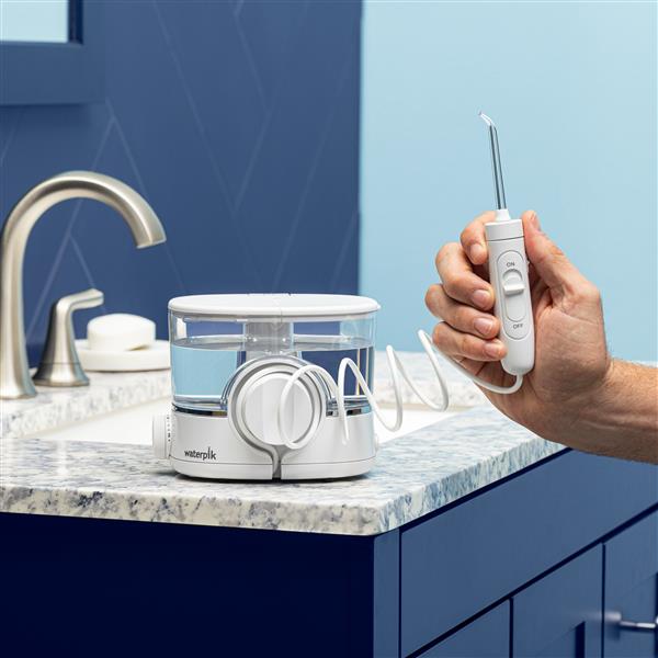 White ION countertop water flosser on a bathroom sink, with hand holding the handle and attached tip, extended by its coiled hose.