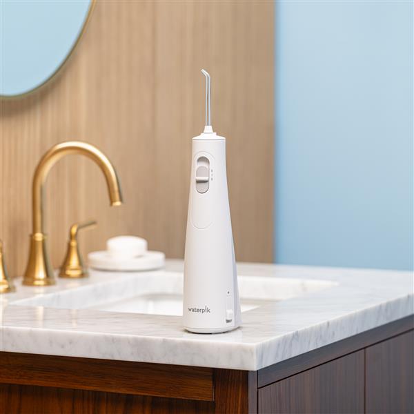 White Cordless 1100 handheld water flosser on a bathroom sink.