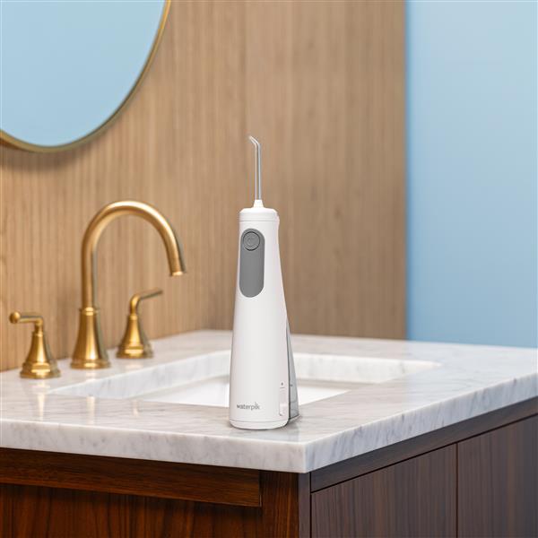 White Cordless Enhance 3200 handheld water flosser on a bathroom sink.